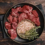 Pedaços de acém cortados em cubos generosos sobre uma superfície de madeira, prontos para o tempero.