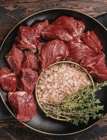 Pedaços de acém cortados em cubos generosos sobre uma superfície de madeira, prontos para o tempero.