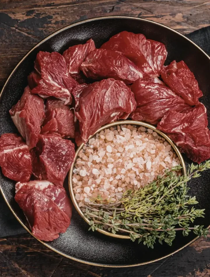 Pedaços de acém cortados em cubos generosos sobre uma superfície de madeira, prontos para o tempero.