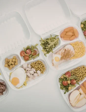 Potes de vidro com divisórias contendo porções equilibradas de proteínas, carboidratos e vegetais.